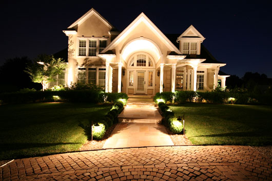Large white home with landscaping and exterior lighting.