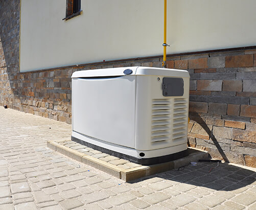 Generac generator installed outside next to a white and brick home.