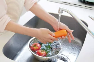 Woman washing vegetables in the kitchen sink with the faucet running.