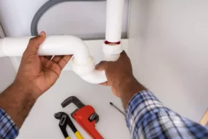 Hands of a plumber fixing a white pipe.