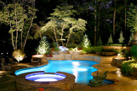 Large natural-shaped pool with in-pool and exterior lighting and landscaping around it.