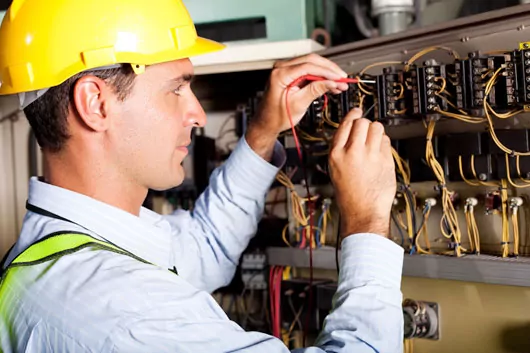 Electrician in yellow hardhat repairing an electrical panel.