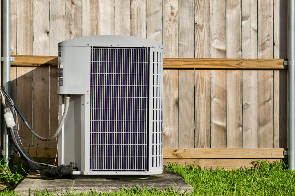 New air conditioning unit installed outside, next to a wooden fence.