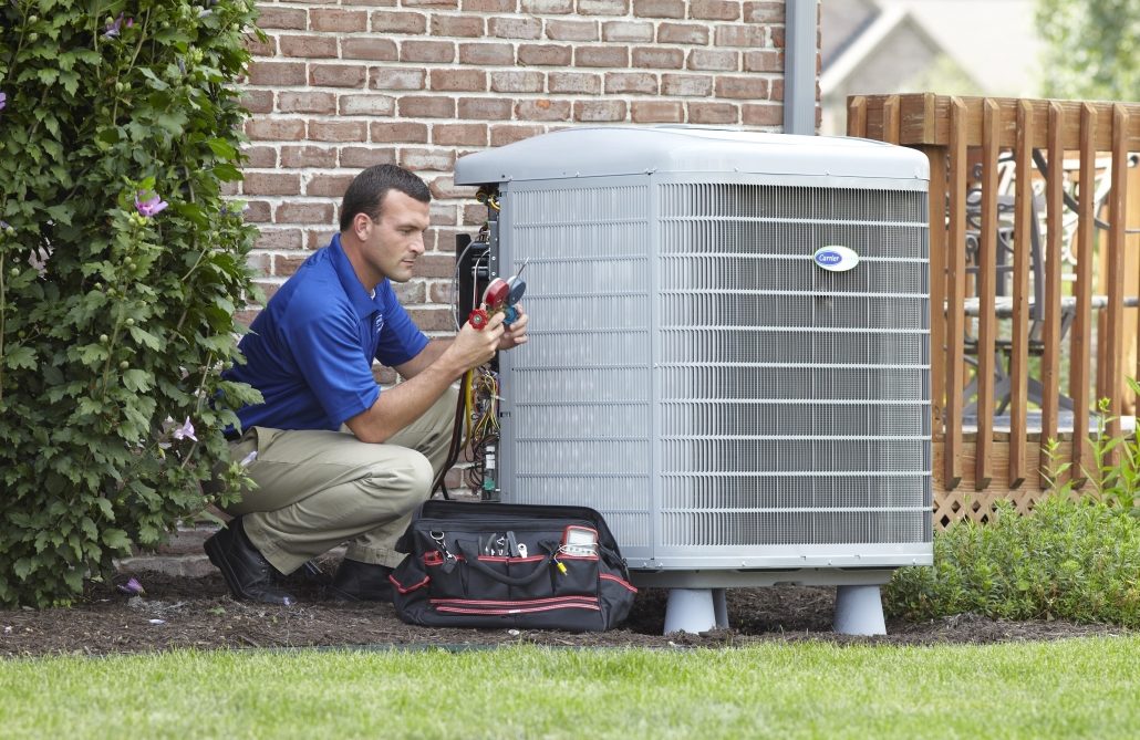 Technician servicing outdoor HVAC unit next to brick home.